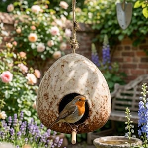 May include: A hanging, speckled birdhouse with a small bird inside. The birdhouse is suspended by a rope. The background includes a garden with flowers, a brick wall, and a bird bath.