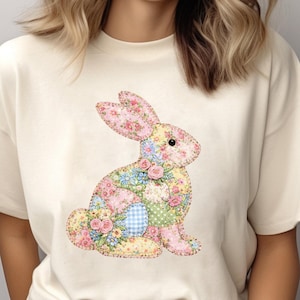 May include: Cream-colored t-shirt featuring a patchwork bunny design. The bunny is adorned with floral patterns in pink, yellow, and blue. The design has a whimsical, springtime aesthetic, perfect for Easter or everyday wear.