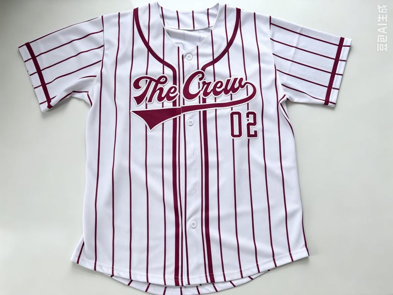 Puede incluir: Una camiseta de b&eacute;isbol blanca de manga corta con rayas verticales de color granate, cierre frontal de botones y el texto The Crew junto al n&uacute;mero 02 impreso en granate en el pecho, con ribetes granates en el cuello y los pu&ntilde;os.