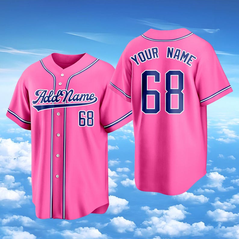 Puede incluir: Una camiseta de b&eacute;isbol de color rosa brillante con ribetes y letras en azul oscuro. La parte delantera muestra el texto Add Name y el n&uacute;mero 68. La parte trasera muestra el texto YOUR NAME sobre el n&uacute;mero 68 con cierre de botones.