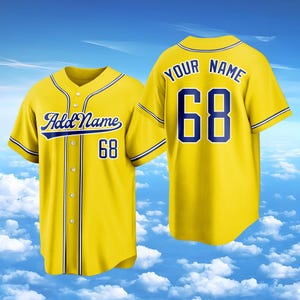 Puede incluir: Una camiseta de b&eacute;isbol de color amarillo brillante con cierre de botones, mangas cortas y ribetes azul oscuro. El frente muestra el texto Add Name y el n&uacute;mero 68, mientras que la parte posterior presenta el texto YOUR NAME y el n&uacute;mero 68.