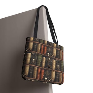 May include: Tote bag featuring a bookshelf design with vintage books, skulls, and cobwebs. The bag has black handles and a dark background. The design includes various book colors, including brown, orange, and green.