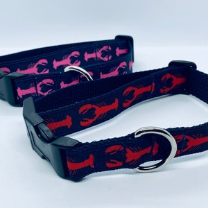 May include: Two dog collars with lobster designs. The top collar has pink lobsters on a black background. The bottom collar has red lobsters on a black background.