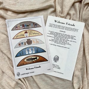 May include: A sewing pattern titled Welcome Friends by Cabbage Rose, featuring five semi-circular applique designs including houses, a boat, snowmen, and a fish. The instruction sheet lists supplies for a finished size of 27.5 inches by 7 inches.