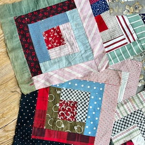 May include: A collection of square fabric quilt blocks featuring a log cabin pattern. The blocks are constructed from various cotton textiles in red, blue, green, black, and white, showcasing diverse prints including stripes, polka dots, and floral motifs.