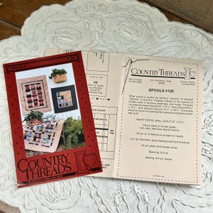 May include: A red brochure titled "Spools #126" by Country Threads, featuring quilt patterns. The brochure displays images of finished quilts and includes detailed instructions and material lists for various projects. The brochure is open, revealing text.