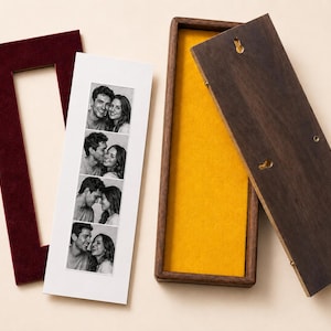 May include: A rectangular dark wood display box with a bright yellow interior lining, a matching dark wood lid with two keyhole slots, and a separate maroon velvet mat frame containing a vertical photo strip of a couple in black and white.