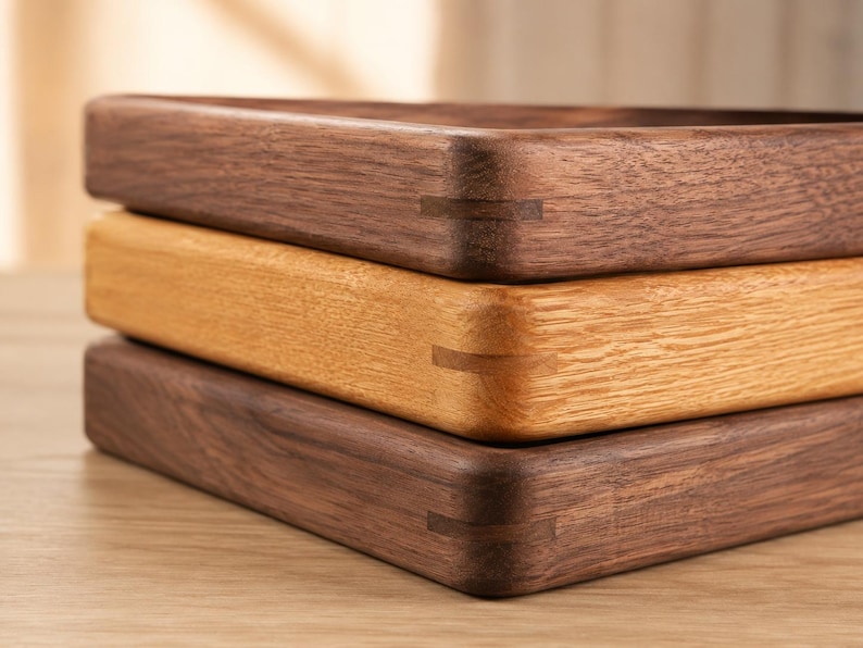 May include: A stack of three rectangular wooden trays with rounded corners. The top and bottom trays are made of dark brown walnut wood, while the middle tray is made of light tan oak wood. Each tray features visible spline joinery details.