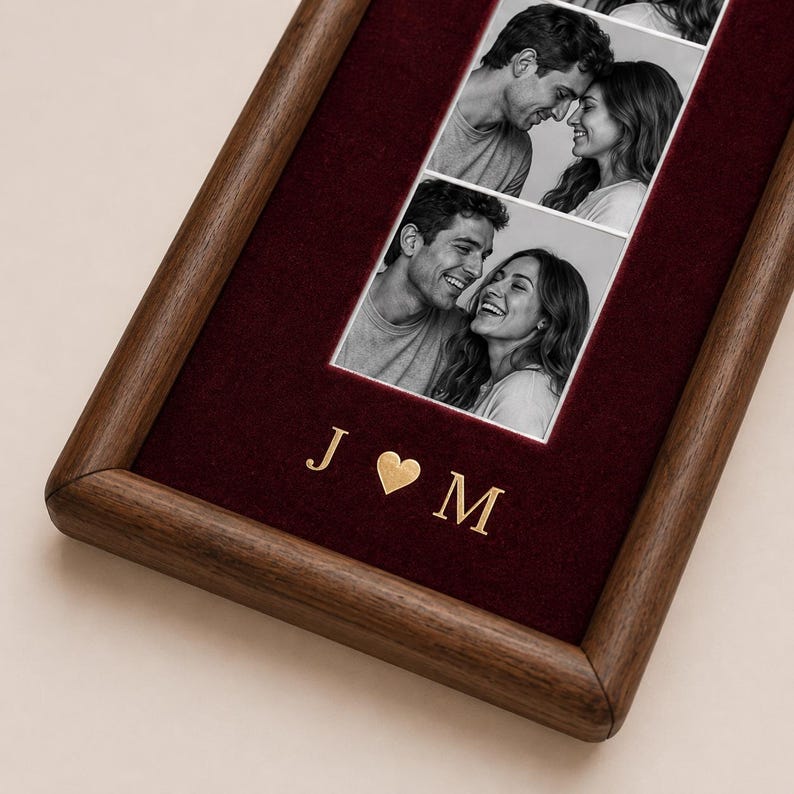 May include: A rectangular wooden picture frame featuring a deep burgundy velvet backing. The frame displays two black and white photographs of a couple. Below the photos, the gold-colored letters J and M are separated by a gold heart symbol.