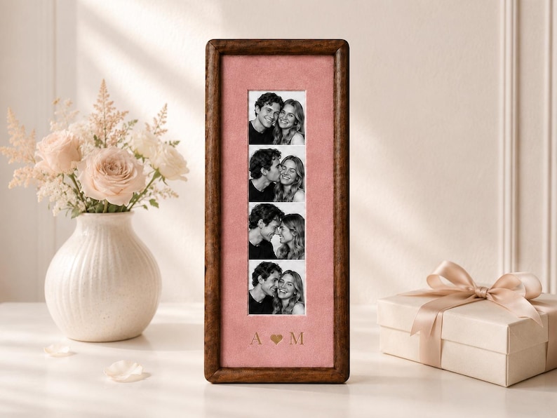 May include: A tall, rectangular wooden picture frame with a dark brown finish, featuring a vertical strip of four black and white photographs of a couple. The photos are set against a dusty pink mat with the gold-colored letters A and M separated by a heart.