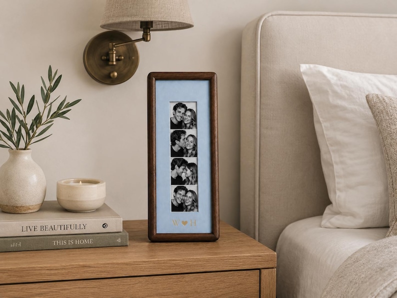 May include: A vertical rectangular dark wood photo frame with a light blue mat board. The frame displays a strip of four black and white photographs of a couple. Below the photos, the letters W and H are separated by a small heart symbol.