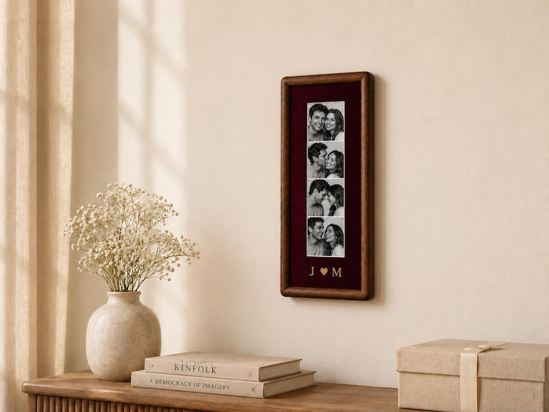 May include: A rectangular dark wood picture frame containing a vertical strip of four black and white photographs of a couple. Below the photos, the letters J and M are separated by a heart symbol in gold lettering on a deep burgundy background.