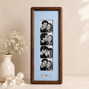 May include: A vertical rectangular dark wood picture frame containing a light blue mat board with four stacked black and white photographs of a couple. The mat board features the gold-colored letters W and H separated by a heart symbol.