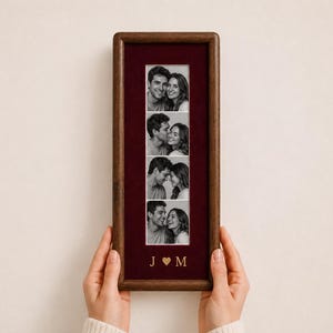 May include: A rectangular dark wood picture frame featuring a deep burgundy velvet mat. The frame displays a vertical strip of four black and white photographs of a couple. Below the photos, the gold letters J and M are separated by a heart.