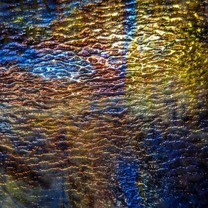 May include: A close-up of a textured glass panel with a vibrant, iridescent surface. The colors shift from deep blues and purples to warm golds and oranges, creating a dynamic, abstract effect. The glass has a rippled texture.