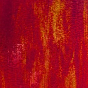 May include: A rectangular piece of stained glass with a fiery red and yellow color scheme. The glass has a textured appearance, with streaks of yellow and orange running through the red base. The glass is held up against a clear blue sky.