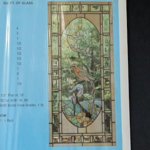 May include: A rectangular stained glass panel featuring an oval center with a bird perched on a branch among flowers and leaves. The panel has a geometric border and is displayed on a light blue background with text listing materials like 1/2" Flat H, 12' and 60/40 Solid Core Solder, 1 lb.