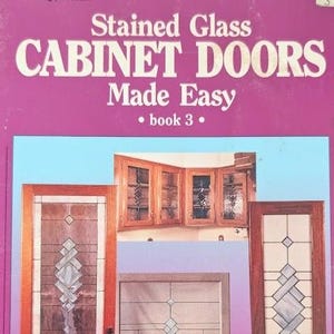 May include: A softcover instructional book titled Stained Glass CABINET DOORS Made Easy book 3. The magenta cover features a light blue rectangular inset displaying photographs of wooden cabinet doors with various stained glass panel designs.