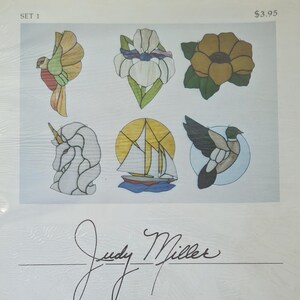 May include: A collection of six stained glass patterns labeled SET 1, featuring a bird, an iris, a flower, a unicorn, a sailboat, and a duck. The designs are printed on a white sheet with the signature Judy Miller at the bottom and a price of $3.95.