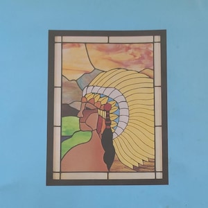 May include: A rectangular stained glass panel featuring a profile view of a person wearing a large yellow feathered headdress. The background depicts a landscape with mountains and a sunset sky in shades of orange, yellow, and green, all framed by black lines.