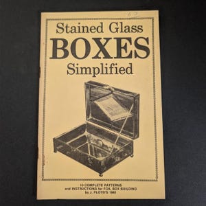 May include: A beige instructional booklet titled Stained Glass BOXES Simplified, featuring a black line drawing of an open glass box on the cover. The text includes 10 COMPLETE PATTERNS and INSTRUCTIONS for FOIL BOX BUILDING by J. FLOYD'S 1981.
