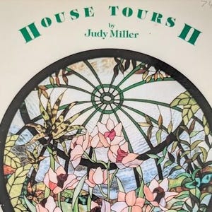 May include: A circular stained glass panel featuring a greenhouse structure with green metal framing, pink orchid flowers, and green foliage. The text "HOUSE TOURS II by Judy Miller" is printed in green above the circular glass artwork.