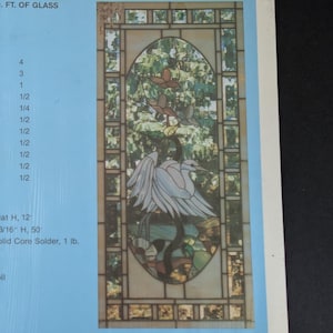 May include: A rectangular stained glass panel featuring an oval center design with a white heron standing among green foliage and brown flowers. The border consists of geometric glass segments in shades of cream, tan, and brown, set in dark metal cames.