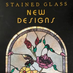 May include: A book cover with the text STAINED GLASS NEW DESIGNS in gold lettering on a black background. Below the text is an arched stained glass window panel featuring red and purple roses, green leaves, and yellow flowers.