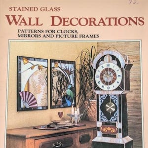May include: A book cover titled STAINED GLASS WALL DECORATIONS PATTERNS FOR CLOCKS, MIRRORS AND PICTURE FRAMES. The cover features a tall stained glass grandfather clock, two framed stained glass wall panels, and a wooden table with a glass.