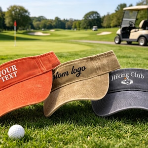 May include: Three sun visors in orange, tan, and dark gray with a distressed fabric texture. The orange visor features the white text "YOUR TEXT", the tan visor has "custom logo" in black, and the dark gray visor displays "Hiking Club".