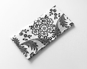 May include: A rectangular, folded fabric item with a black and white floral pattern. The design features large, stylized flowers and foliage against a white background. The edges are neatly finished, suggesting a decorative or functional textile.
