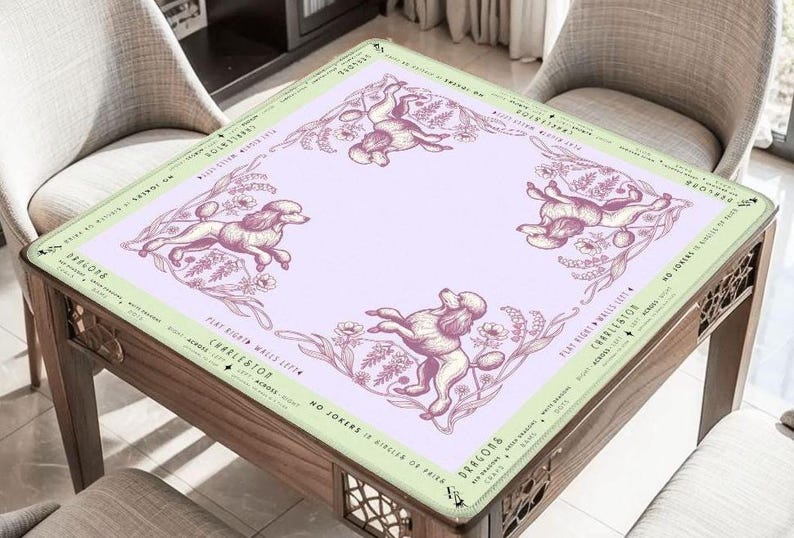 May include: A square table with a light purple surface featuring illustrations of poodles and floral elements. The table's border is light green with text. The table is made of wood and has decorative cutouts on the sides.
