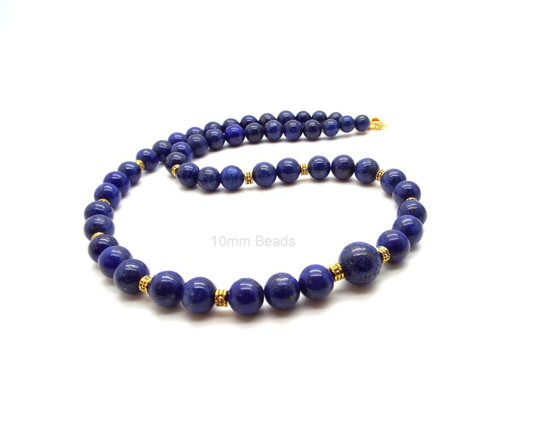 May include: A necklace featuring deep blue lapis lazuli beads, approximately 10mm in diameter, strung together with gold-colored spacers. The necklace is displayed against a white background. The text "10mm Beads" is visible.