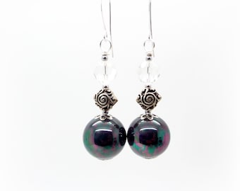 May include: A pair of dangle earrings with a dark green and purple iridescent bead, a silver crystal bead, and a silver filigree charm.