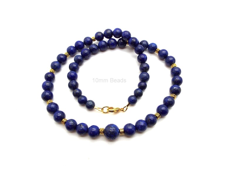 May include: A necklace featuring deep blue, 10mm beads. The beads are strung together with gold-colored accents and a gold clasp. The necklace is displayed on a white background.