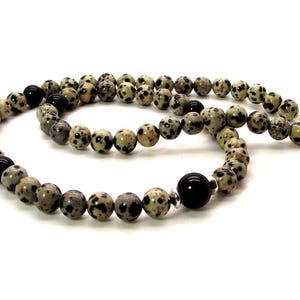 May include: A necklace made of dalmatian jasper beads and black onyx beads. The necklace has a silver clasp.