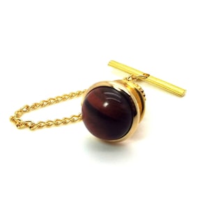 Puede incluir: Un broche de corbata de oro con una piedra de ojo de tigre roja.