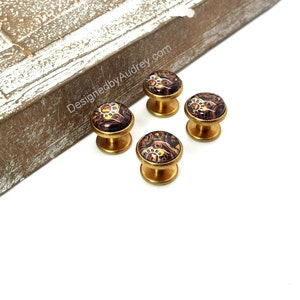May include: Set of four gold-toned cufflinks with a brown and gold patterned design.  The cufflinks are on a white surface.