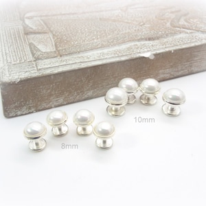 May include: A set of pearl buttons in two sizes, 8mm and 10mm. The buttons are white and have a silver base.