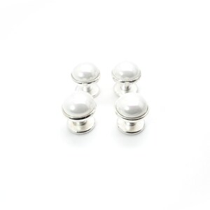 May include: Four white pearl cufflinks with silver settings. The cufflinks are arranged in two rows of two.