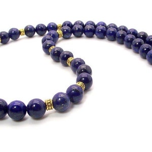 May include: A necklace featuring deep blue, spherical beads. The beads are separated by gold-colored spacers and are strung together. The necklace is secured with a gold-colored clasp. The jewelry is displayed against a white background.
