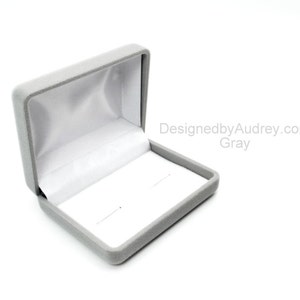 May include: A gray velvet jewelry box with a white satin interior. The box is open and the lid is propped up.
