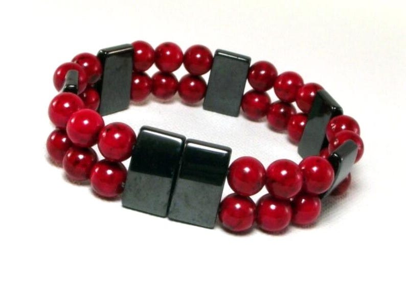 May include: A double-strand bracelet with red beads and black rectangular magnetic clasps.