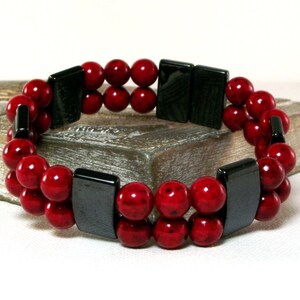 May include: A double-strand bracelet with red beads and black rectangular spacers.