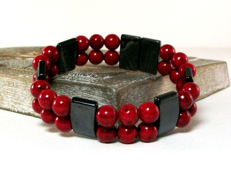 May include: A double-strand bracelet with red beads and black rectangular spacers.