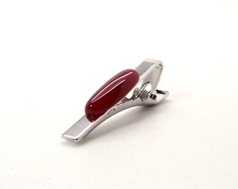 May include: A silver tie clip with a red oval-shaped stone.