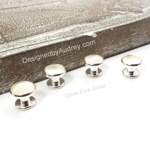 May include: Four silver and white 10mm fine silver shirt buttons. The buttons have a round, white top and a silver base.