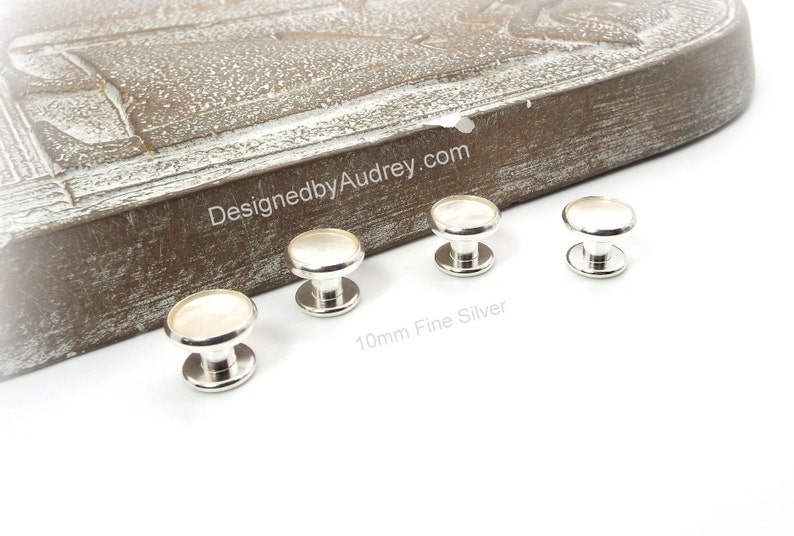 May include: Four silver and white 10mm fine silver shirt buttons. The buttons have a round, white top and a silver base.