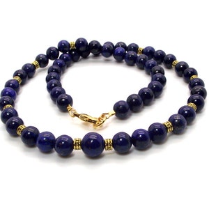 May include: A necklace featuring dark blue, spherical beads. The beads are strung together with gold-colored accents and a gold clasp. The necklace is displayed against a white background, highlighting the jewelry's color and design.