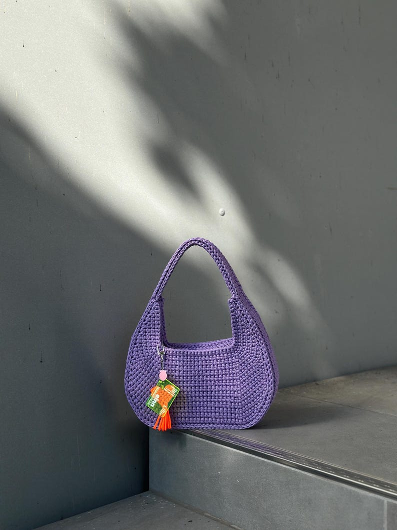 May include: A purple crocheted handbag with a small orange tassel hanging from it. The bag is sitting on a set of stairs.